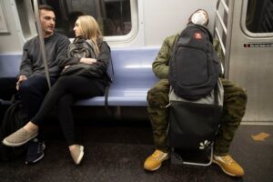 photo of 3 people on a subway car. One is wearing a face mask. Two do not. What should you do if you are returning to public transport? AP Photo by Mary Altaffer, Time, 3/11/2-2020