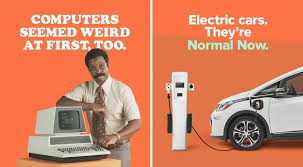 Side by side ad of an early computer and an electric car at a charging station. The point for the EV is that we learn a "new normal". From the Electrify America Ad campaign.